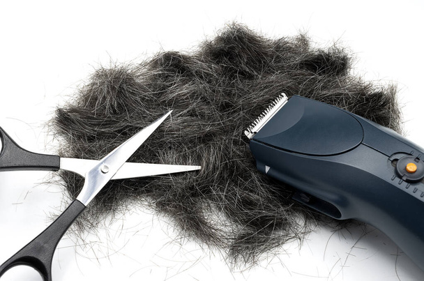 Una cortadora de cabello, tijeras y pelo gris cortado sobre fondo blanco - Foto, Imagen