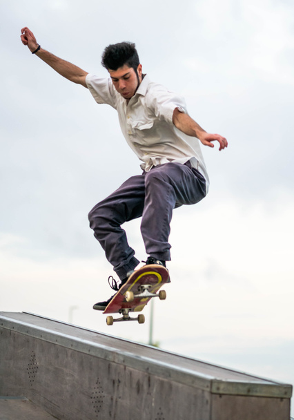 Um jovem caucasiano fazendo truques com um skate em um parque de skate - Foto, Imagem