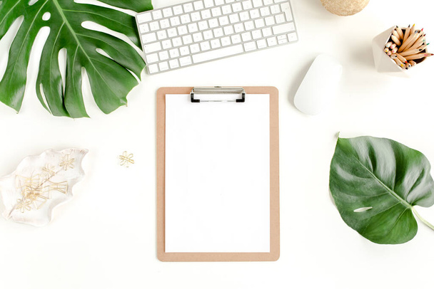 Flat lay home office desk. Female workspace with computer, clipboard, tropical palm leaves Monstera, accessories on white background. Top view.  - 写真・画像