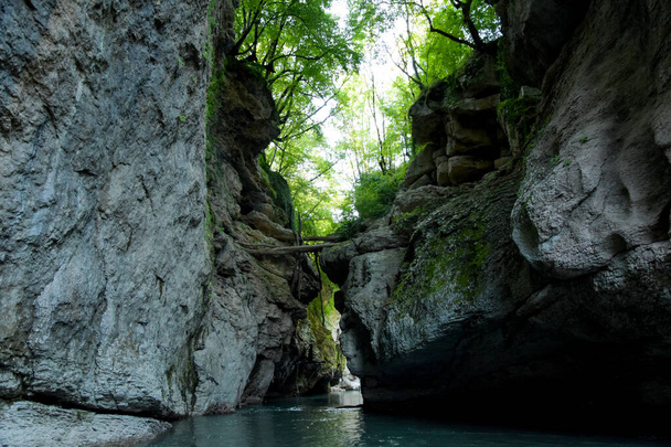 Entre as rochas altas, um rio de montanha azul flui no desfiladeiro. As rochas são cobertas de floresta, formam uma paisagem pitoresca. - Foto, Imagem