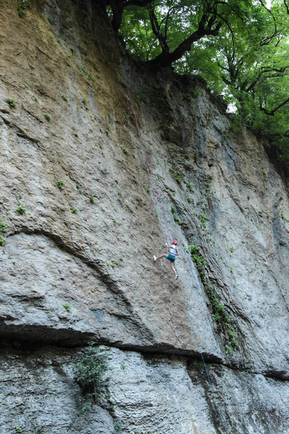 Een klimmer in uniform gaat een grijze rots in. De atleet beklimt de rots met behulp van de touwen. - Foto, afbeelding