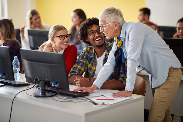 Female cheerful professor with pupils looking in computer - Foto, afbeelding