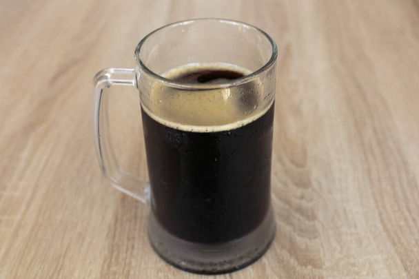 La tazza umida di una birra scura fresca su un tavolo di legno nel pub. - Foto, immagini