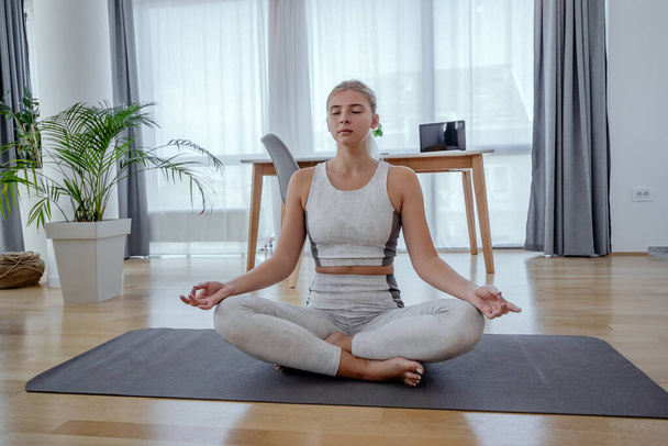 Kaunis aktiivinen nuori nainen meditoi jooga Asana Lotus aiheuttaa kotona. Terveellinen elämäntapa ja urheilukonsepti. Harjoitussarja aiheuttaa. - Valokuva, kuva