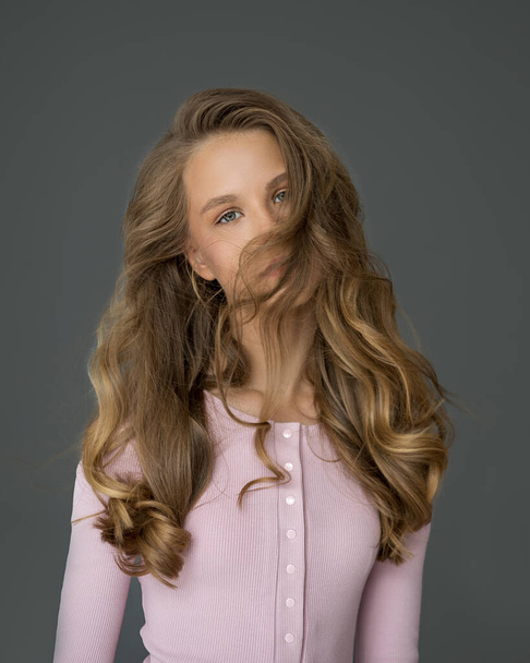 Stüdyoda gri arka planda dalgalı saçları olan güzel esmer bir kızın portresi. Rüzgâr. Saç bakımını kavra - Fotoğraf, Görsel