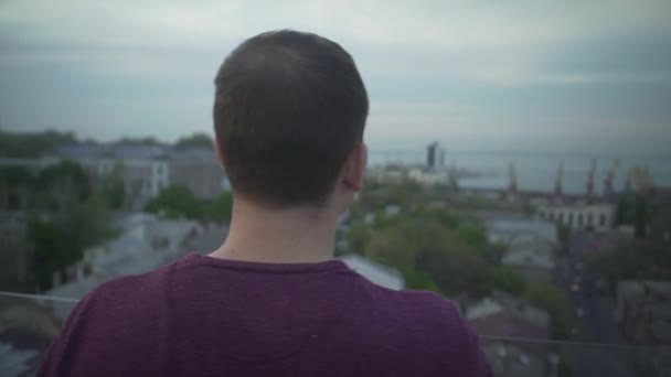 Крупним планом панорамний вид на пташине око на темноволосих чоловіка, що стоїть на краю даху мріє дивитися на морську гавань
 - Кадри, відео