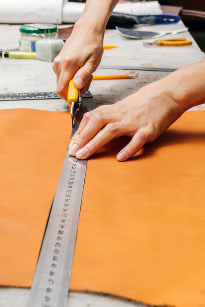 persons hands using cutting tool and metal ruler while producing leather goods - Фото, изображение