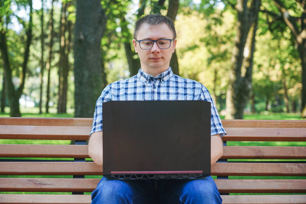 The guy sits on a park bench and works at a laptop. - Zdjęcie, obraz