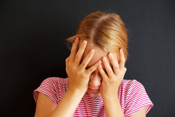 Teenagermädchen hält kranken Kopf mit den Händen, Porträt auf schwarzem Hintergrund. - Foto, Bild