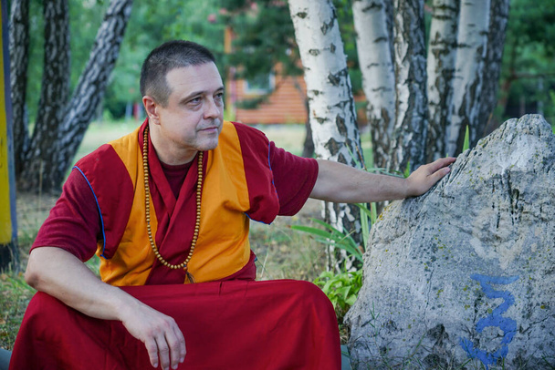 lama monnik met een houten rozenkrans rond zijn nek chides in de buurt van een grote steen - Foto, afbeelding