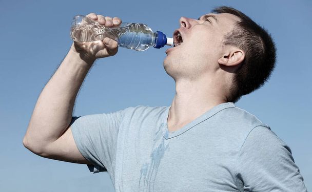 парень в очках и футболке держит в руках пластиковую бутылку с водой - Фото, изображение