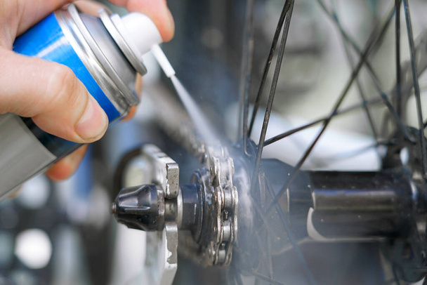 lubricante en aerosol de mano en su mano para lubricar la cadena de la bicicleta - Foto, Imagen