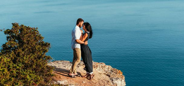 A couple in love embraces on the beach. A happy couple meets the dawn by the sea. Honeymoon trip. The couple is having fun by the sea. Beautiful couple on the sea. Copy space - Zdjęcie, obraz