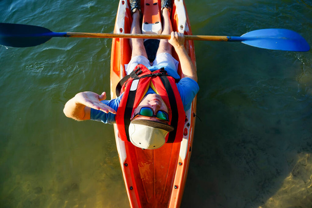 un kayak con gafas sostiene una paleta en sus manos y mira hacia arriba - Foto, Imagen