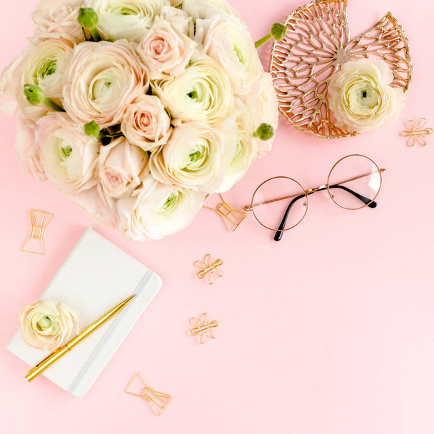 Stylized, pink womens home office desk. Workspace with bouquet ranunculus and roses, clipboard on pink background. Flat lay. Top view. - Photo, Image