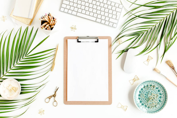 Flat lay home office desk. Female workspace with computer, clipboard, tropical palm leaves, accessories on white background. Top view.  - Фото, изображение