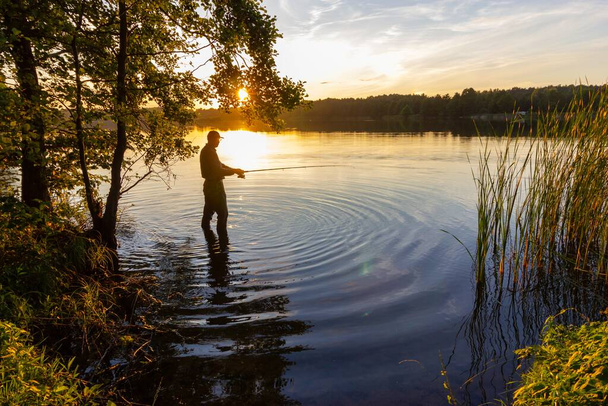Angler catching the fish in the lake during sunset - Foto, immagini