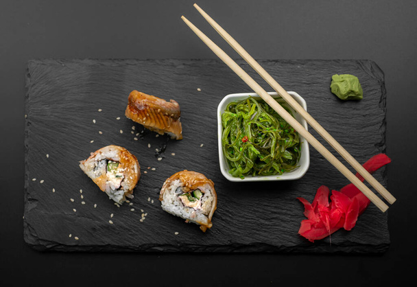 Sushi with eel and wakame hayashi salad lie on a black board made of stone. Top view - Foto, Bild