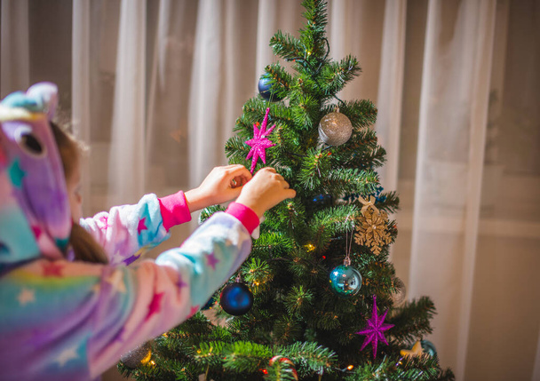  little girl dressed up as a reindeer Rudolf decorating a Christmas tree - Foto, afbeelding