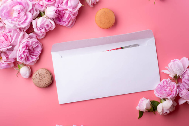  white envelope with card around roses and macaroons against  pink background. life style concept - Valokuva, kuva
