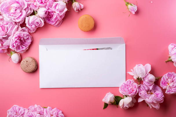  white envelope with card around roses and macaroons against  pink background. life style concept - Foto, imagen