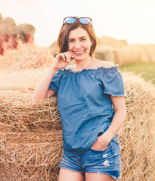 Beatiful woman smiling near haystack on field - Foto, Imagen