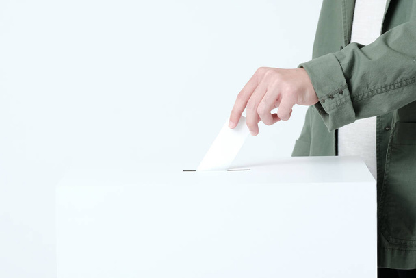 Hände eines jungen Mannes, der einen Stimmzettel in eine Wahlurne wirft - Foto, Bild