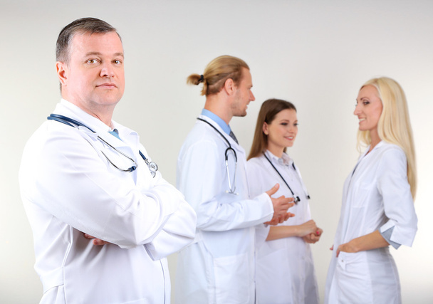 Doctor standing in front of coworkers on grey background - Photo, image
