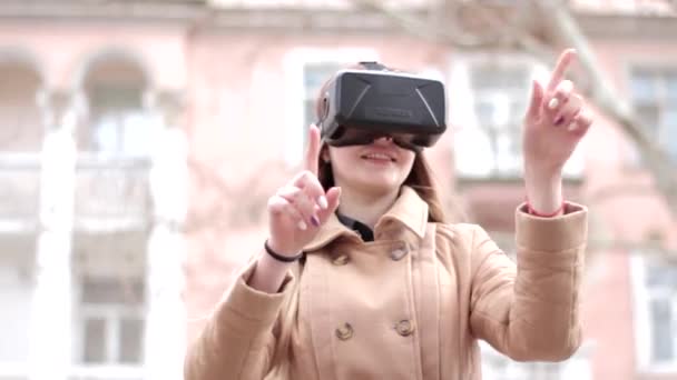 Szczęśliwa kobieta w technologii cyberprzestrzeni wirtualnej rzeczywistości VR okulary słuchawkowe w beżowym płaszczu bielizny bawiąc się na zewnątrz na ulicy - Materiał filmowy, wideo