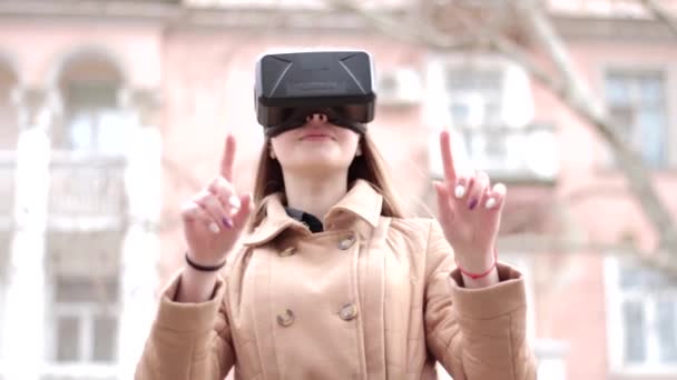 Νεαρή ευτυχισμένη γυναίκα φορώντας τεχνολογία κυβερνοχώρου εικονική πραγματικότητα vr γυαλιά ακουστικά σε μπεζ παλτό outwear διασκεδάζοντας έξω στο δρόμο - Πλάνα, βίντεο