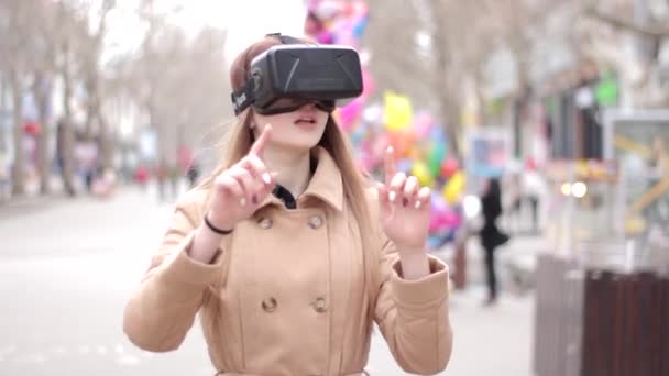Молода дівчина в гарнітурі віртуальної реальності в окулярах кіберпростору весело грає на вулиці в бежевому зовнішньому пальто
 - Кадри, відео