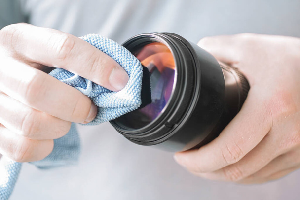 hand houdt een microvezel doek voor het reinigen van de lens van de dslr camera veegt stof van de lens glas - Foto, afbeelding
