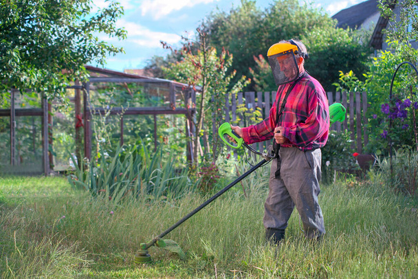 Bir adam evinin yanında elektrikli çim biçme makinesiyle çim biçiyor. - Fotoğraf, Görsel