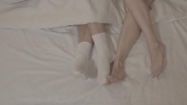 Çıplak ayakla yatakta uzanan iki kadın beyaz çoraplı erkek bacaklarına dokunuyor. - Video, Çekim