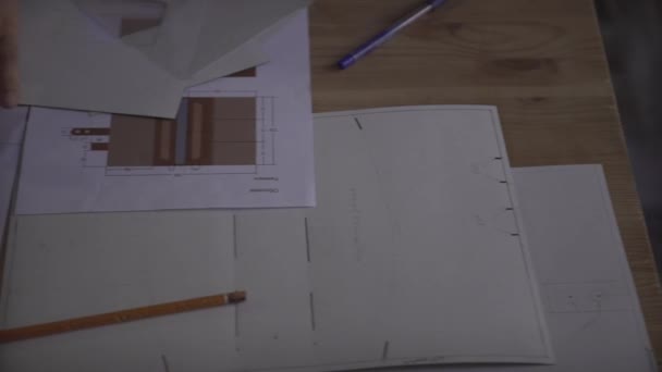 Praca człowieka starannie koncentruje się na drobnych szczegółach projektu pracy papierniczej na drewnianym stole - Materiał filmowy, wideo