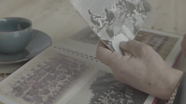 Nahaufnahme von alten Frauenhänden, die auf einem Schwarz-Weiß-Foto in einem Familienalbum auf einem Holztisch auf junge Menschen zeigen - Filmmaterial, Video