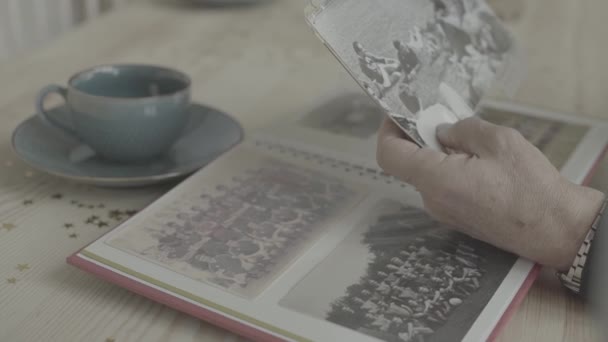 Old woman hands pointing at young people on black white photograph in family photo album on wood table in close up view - Footage, Video