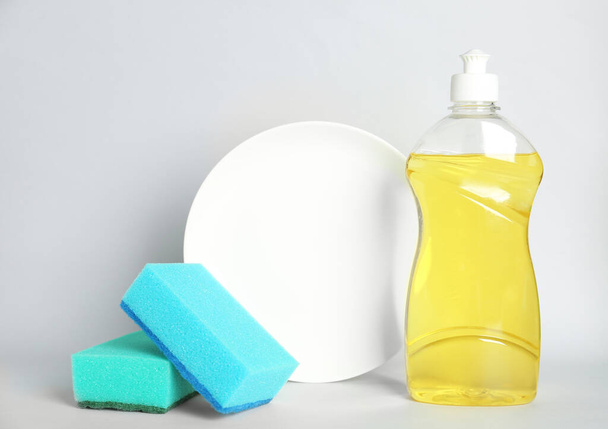 Detergent, plate and sponges on light background. Clean dishes - Fotoğraf, Görsel