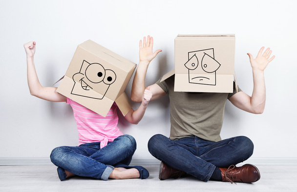 Couple with cardboard boxes on their heads sitting on floor near wall - Foto, afbeelding