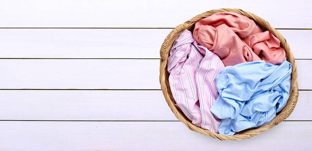 Vestiti colorati in cesto della lavanderia su sfondo bianco in legno. Copia spazio - Foto, immagini