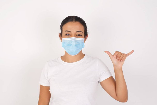 Young arab woman wearing medical mask standing over isolated white background showing up number six Liu with fingers gesture in sign Chinese language - Fotó, kép