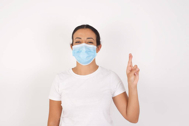 Junge arabische Frau mit medizinischer Maske steht vor isoliertem weißen Hintergrund und zeigt mit den Fingern Nummer zehn in der chinesischen Zeichensprache Shi nach oben - Foto, Bild
