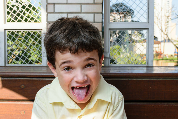 Brazylijskie dziecko w wieku 7 lat, w słoneczne popołudnie, patrząc w kamerę i pokazując swój język. - Zdjęcie, obraz