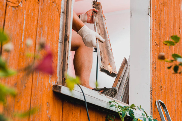 Vervanging van een raam en een raamkozijn, ontmanteling van een oud raam in een privéwoning op het platteland, de arbeider ontmantelt een oud houten raam.2020 - Foto, afbeelding