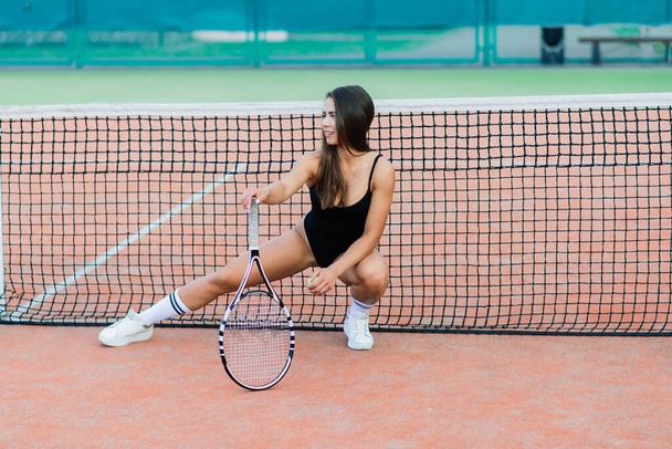 Beautiful young free sports sexy fitness girl dressed in bodysuit, sneakers, with a smart ass and long legs, on a sports ground on a tennis court with a beautiful sky in the background - 写真・画像