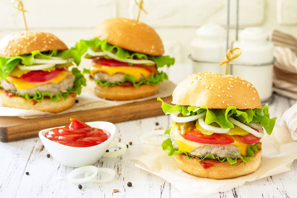 Pyszne hamburgery, kanapka z hamburgerem z kotletem, serem, bekonem i pomidorami na drewnianym stole. - Zdjęcie, obraz