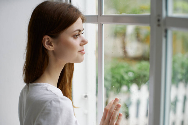 Женщина смотрит в окно интерьера дома утром  - Фото, изображение