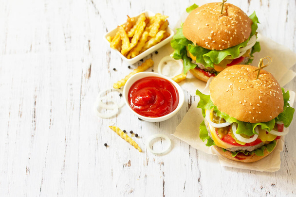 Köstliche hausgemachte Burger mit Schnitzel, Käse, Speck, Tomaten und Pommes auf einem Holztisch. Kopierraum. - Foto, Bild