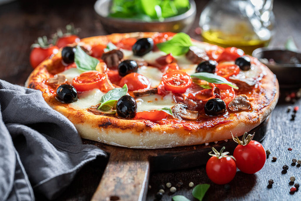 Homemade pizza Capricciosa with mozzarella, prosciutto and tomatoes on wooden table - Fotoğraf, Görsel