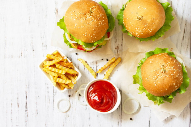 Köstliche hausgemachte Burger mit Schnitzel, Käse, Speck, Tomaten und Pommes auf einem Holztisch. Draufsicht flacher Hintergrund.  - Foto, Bild